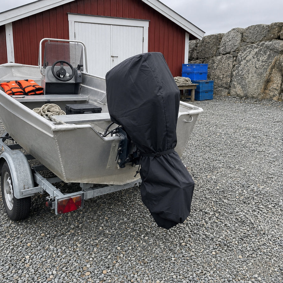Aluminiumbåt på släpvagn med svart motorskydd på utombordaren vid ett rött båthus