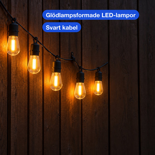 Närbild av tända glödlampsformade LED-lampor på en svart kabel mot en mörk träfasad