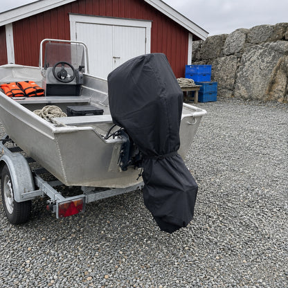 Aluminiumbåt på släpvagn med svart motorskydd på utombordaren vid ett rött båthus