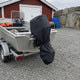 Aluminiumbåt på släpvagn med svart motorskydd på utombordaren vid ett rött båthus