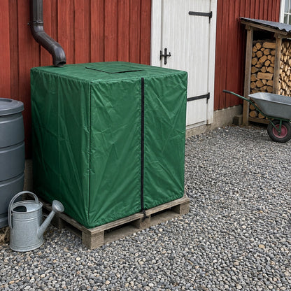 Grönt tanköverdrag över en IBC-tank på pall vid en röd ladugårdsvägg
