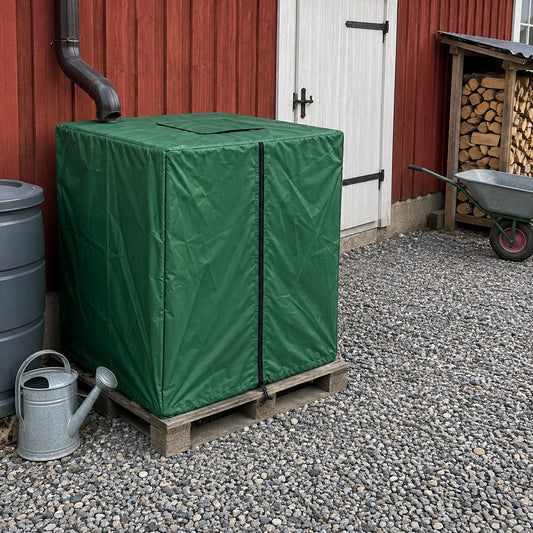 Grönt tanköverdrag över en IBC-tank på pall vid en röd ladugårdsvägg
