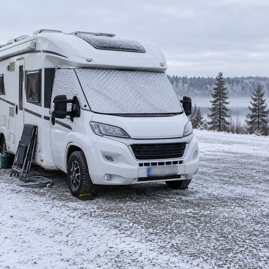 Vit husbil på en snöig grusplan en vintermorgon med silverfärgat termoskydd över vindrutan och sidorutan