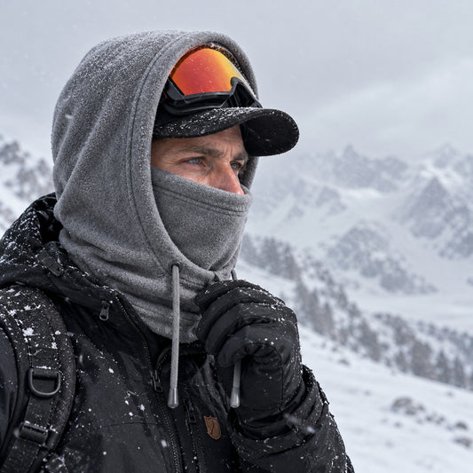 Man i grå fleecebalaklava och keps som håller i dragskon i snöfall på ett fjäll