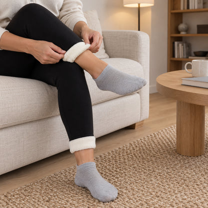 Kvinna i soffa viker upp fållen på svarta leggings vid ankeln så att det krämvita fleecefodret syns