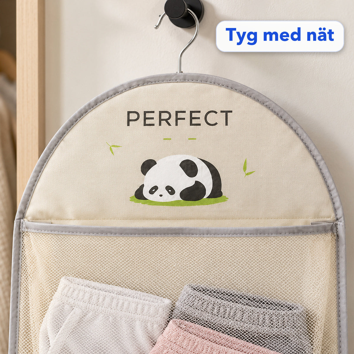 Närbild på förvaringsväskans välvda topp med tryck, kantband och metallkrok samt nätfickans övre del med hopvikta plagg, med texten Tyg med nät