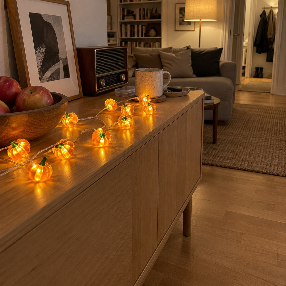 Ljusslinga med tända bärnstensfärgade pumpor längs ett sideboard i ett vardagsrum på kvällen