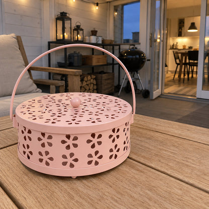 Närbild på rosa myggspiralhållare med blomformade hål i lock och sida på ett bord på en uteplats