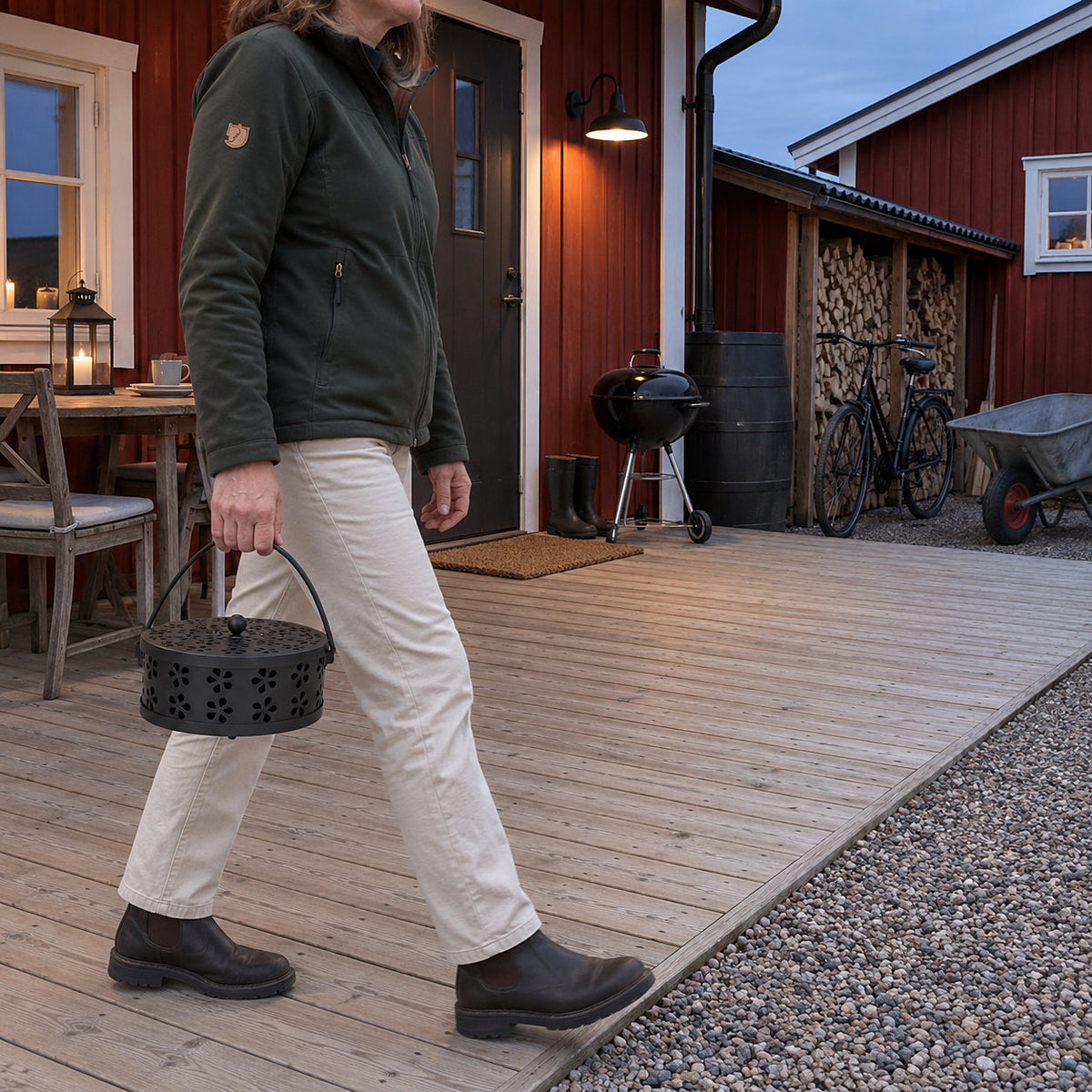 Svart myggspiralhållare som bärs i handtaget över en träaltan vid ett rött hus