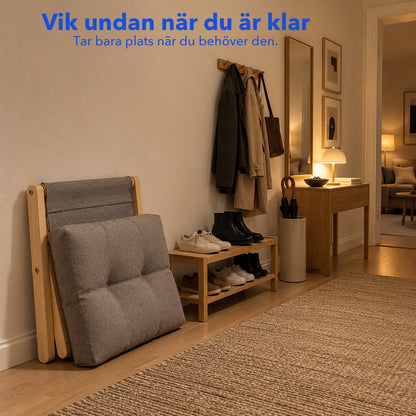 Ihopvikt pall i trä som står mot väggen i en hall med den grå dynan bredvid, med texten Vik undan när du är klar
