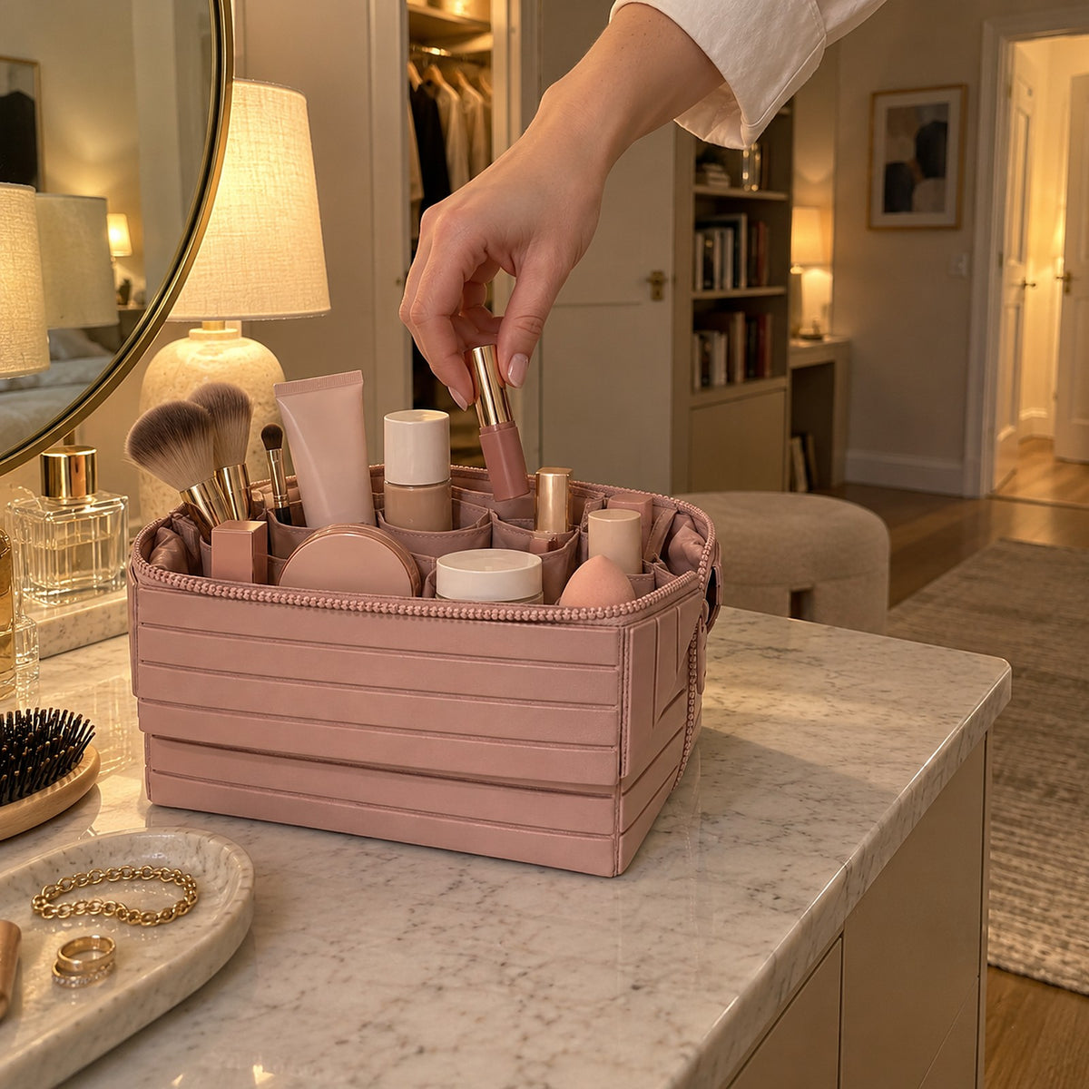 Hand plockar ett läppstift ur en öppen rosa sminkväska med fack på ett sminkbord