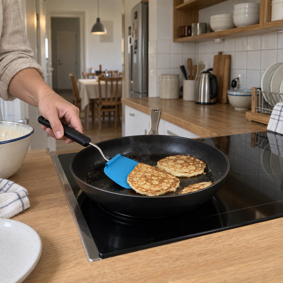 Vinkelbar stekspade med blått blad som lyfter en pannkaka ur stekpannan i ett inrett kök