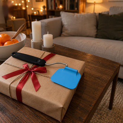 Vinkelbar stekspade med blått blad på ett presentpaket i kraftpapper med rött band på ett soffbord