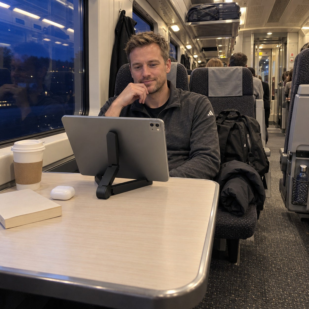 Man på tåget en kväll tittar på en surfplatta som står på det svarta surfplattestället på fällbordet