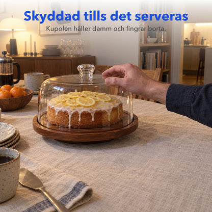 Citrontårta under genomskinlig kupol på träbricka, en hand vilar på kupolen